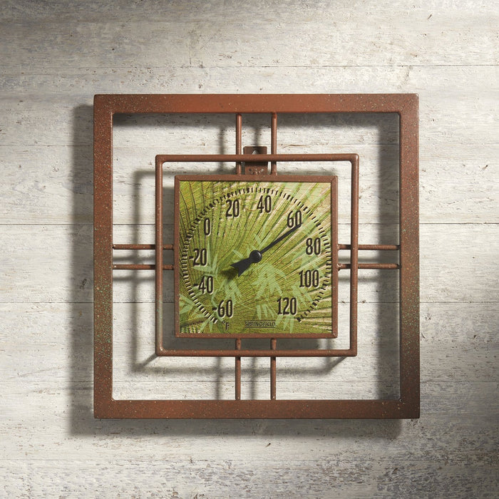 Front view of a decorative bamboo leaf thermometer with antique bronze frame against a rustic wood background