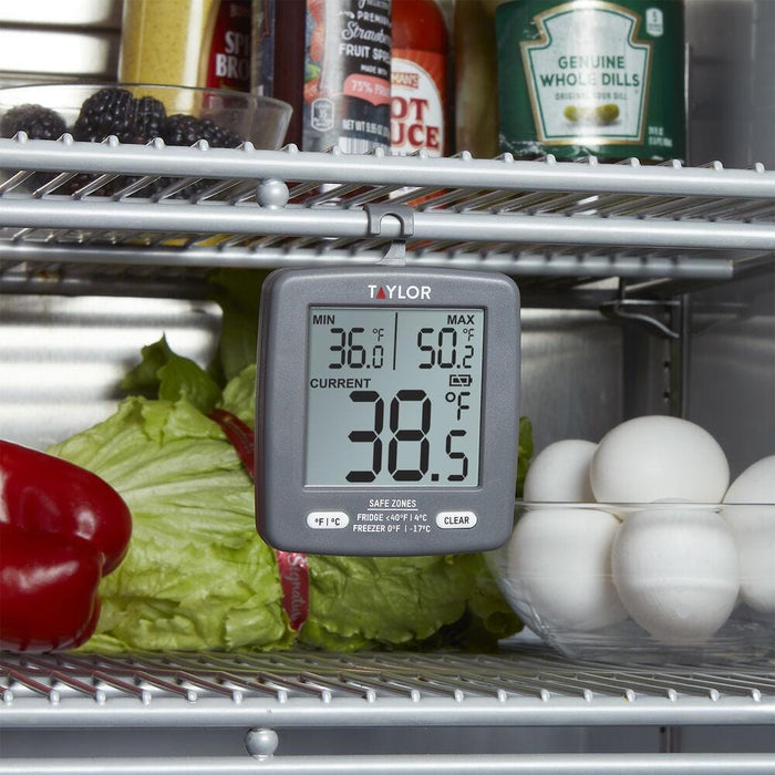 Taylor digital thermometer hanging in a fridge among vegetables and eggs, displaying min 36.0 F max 50.2 F and current 38.5 F.