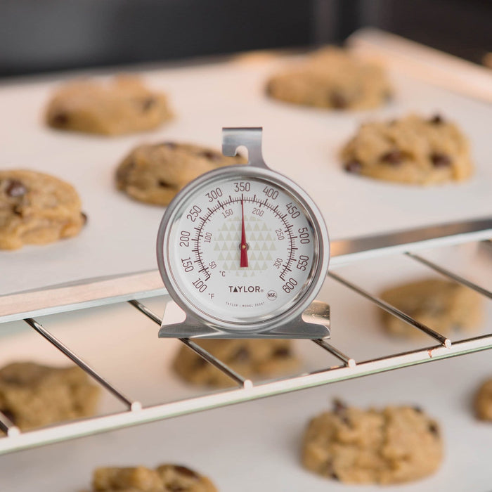 Oven thermometer on a rack with cookies baking in the background